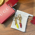 Gold-tone keychain pair with lime and red capsule charms in a white drawstring pouch
