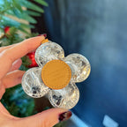 Monogram flower keychain with tan circular badge on the front, held in hand