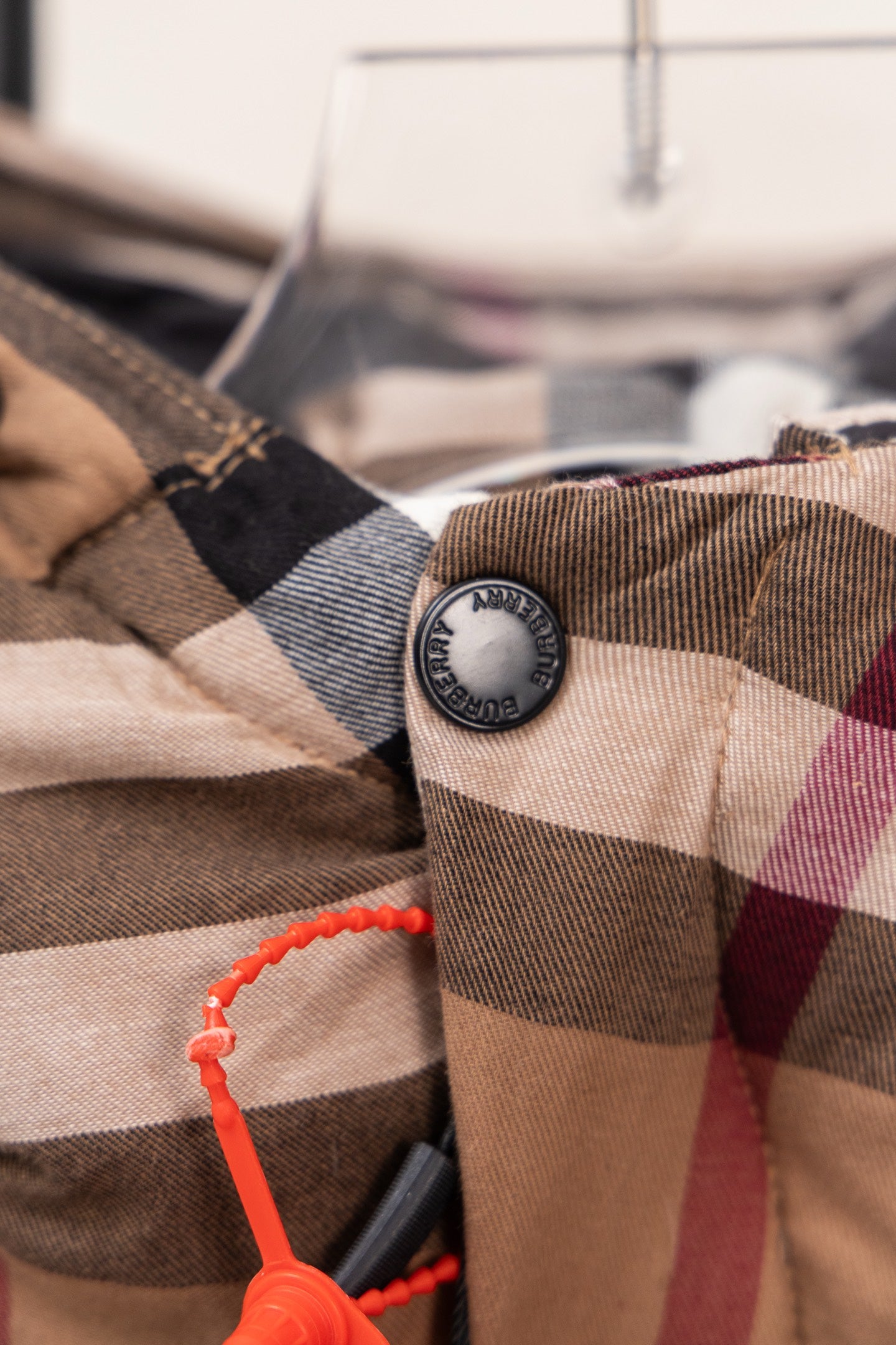 Plaid fabric close-up with round logo button and orange drawcord loop