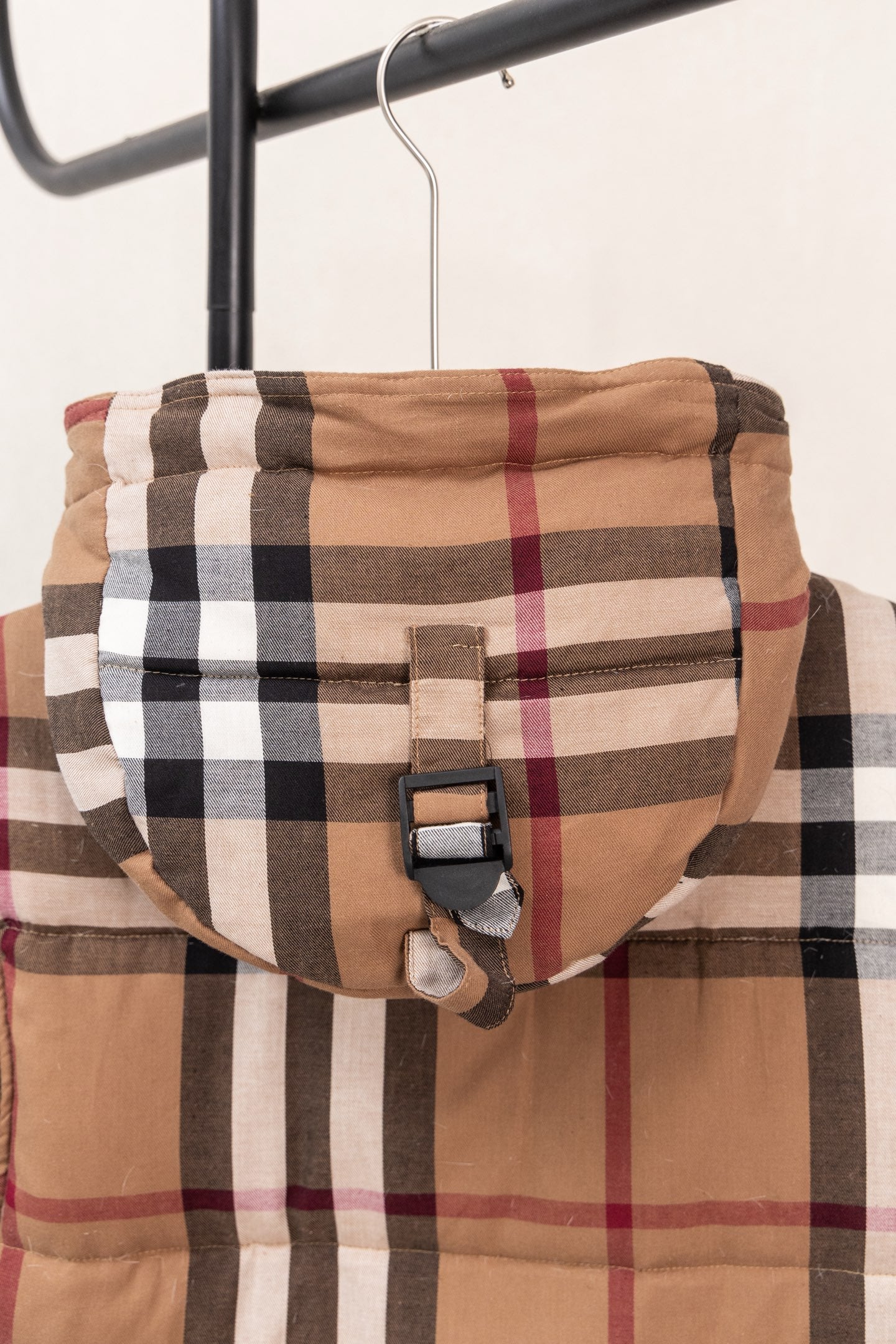 Plaid hooded puffer vest detail with adjustable strap and brown, black, white, and red checks