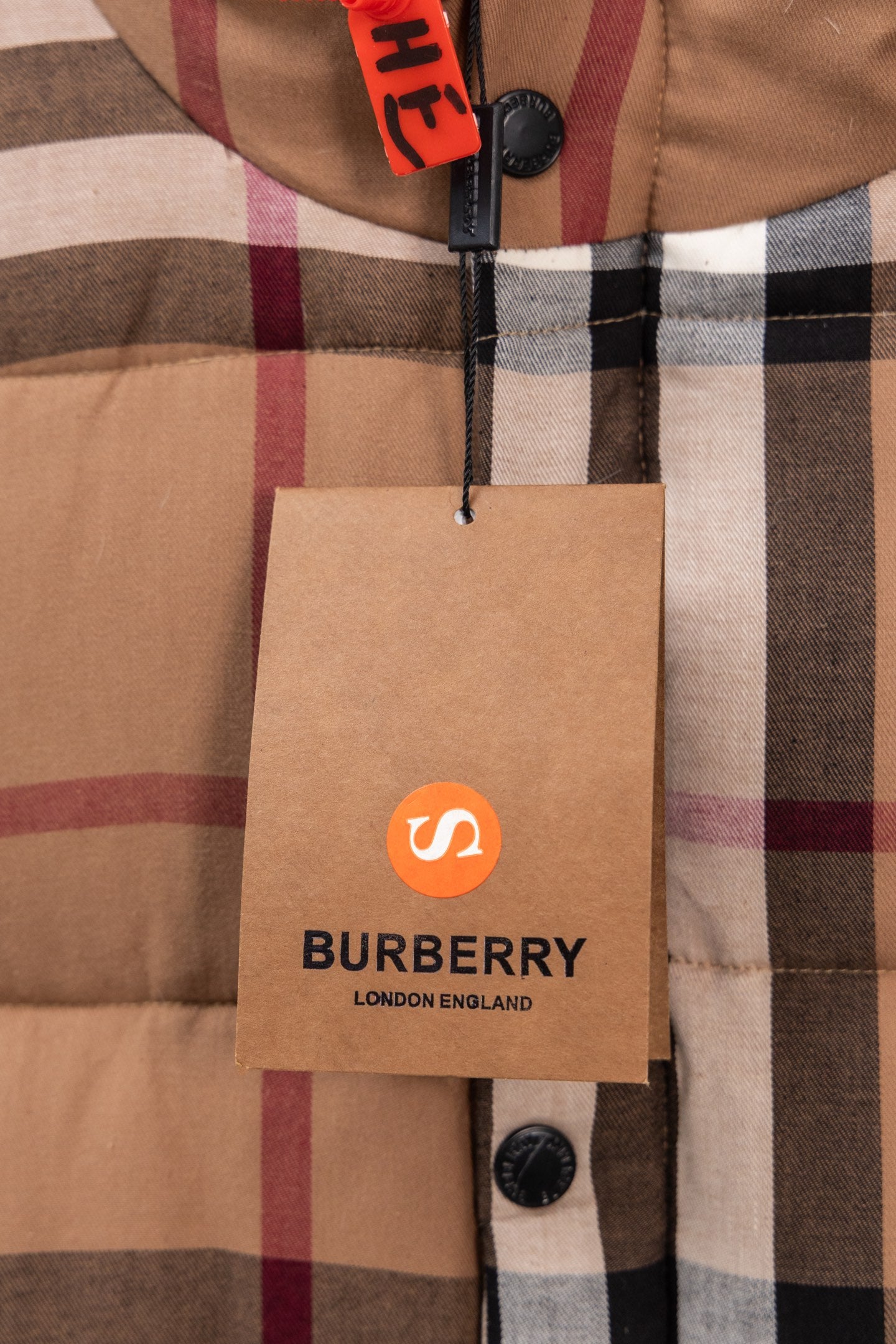 Burberry hang tag on plaid puffer vest with orange and black text, plus zipper pull