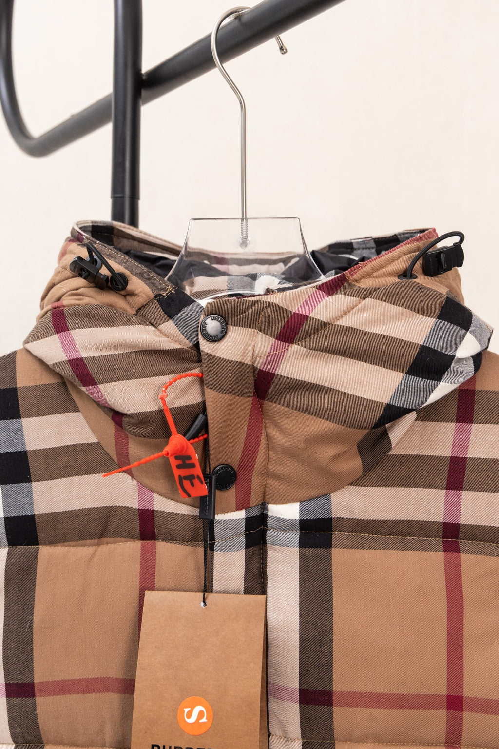 Burberry plaid hooded puffer jacket on a hanger with orange hanging tag