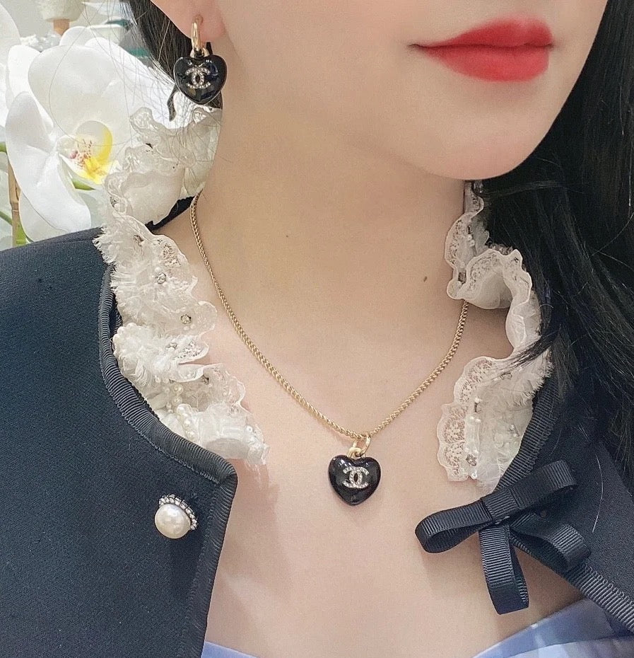Chanel heart charm earrings worn, black resin heart with gold-tone CC emblem.
