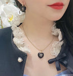 Chanel heart charm earrings worn, black resin heart with gold-tone CC emblem.