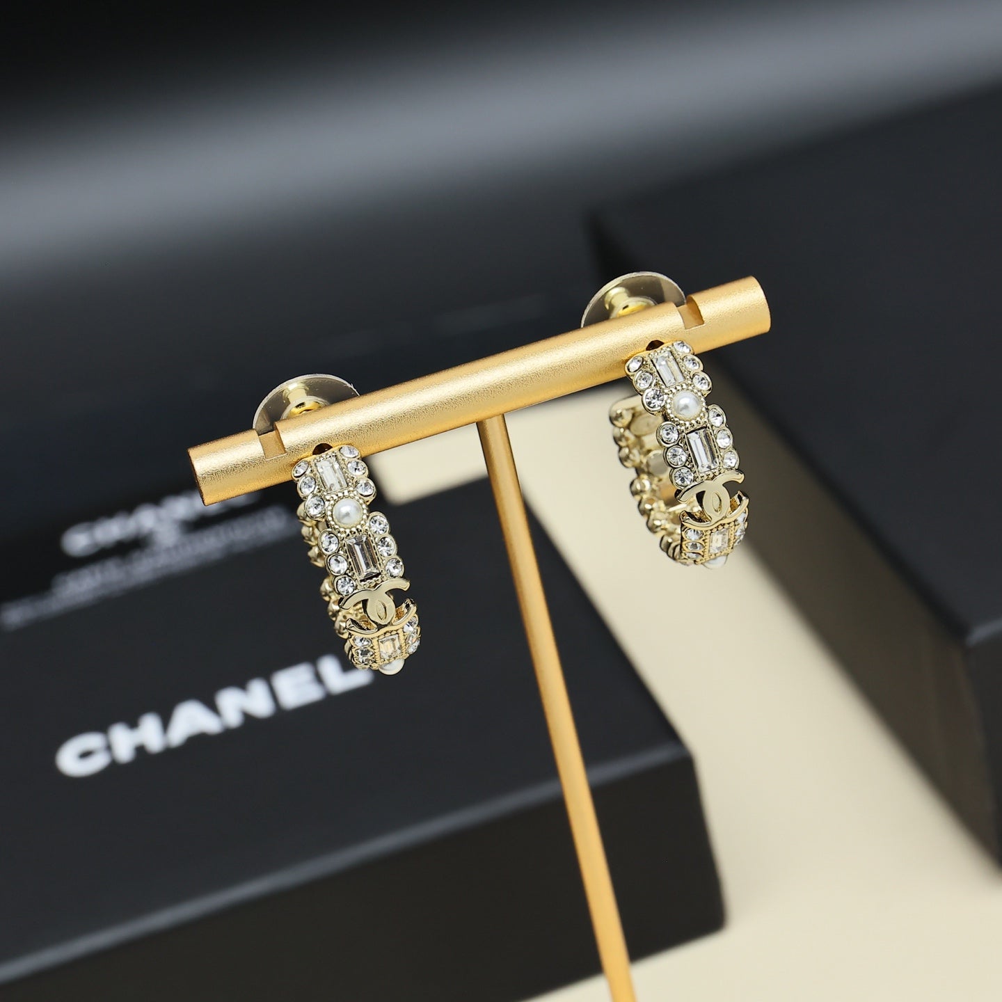 Gold-tone hoop earrings with pearl and rhinestone links on display stand.