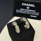 Gold-tone hoop earrings with pearl and rhinestone charms on black jewelry pillow.
