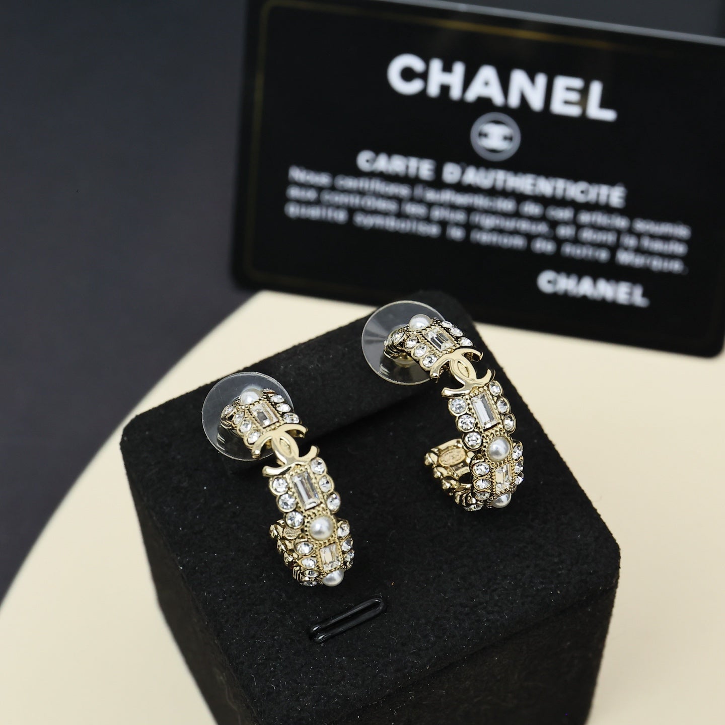 Gold-tone hoop earrings with pearl and rhinestone charms on black jewelry pillow.