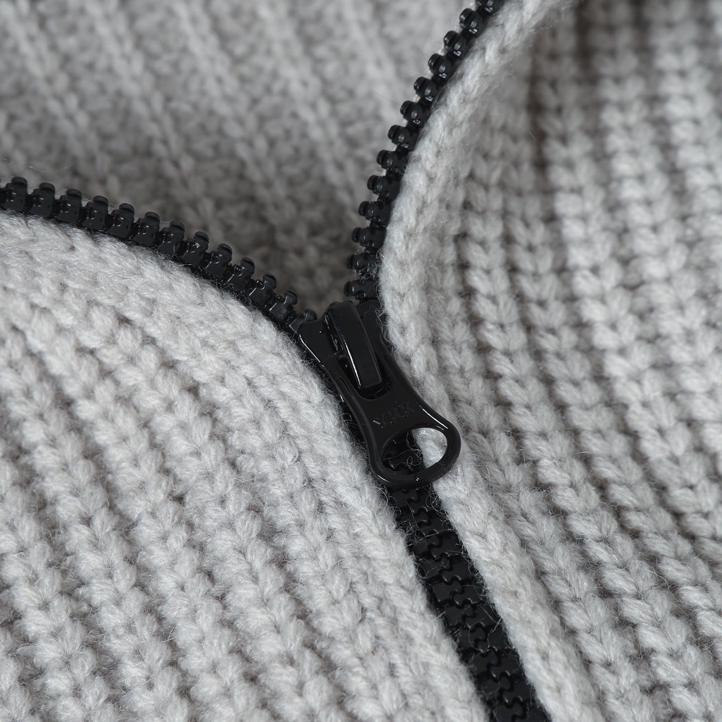 Close-up of light gray knit hoodie with black zipper and pull tab