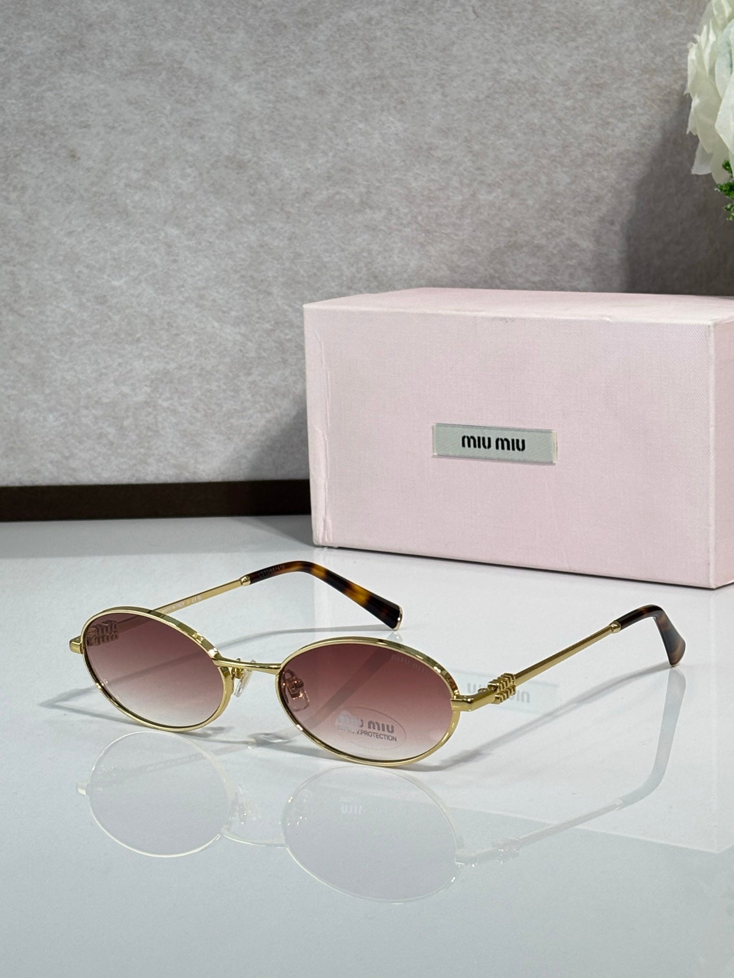 MiuMiu oval eyeglasses with gold-tone metal frame, black temple tips, rose-tinted lenses