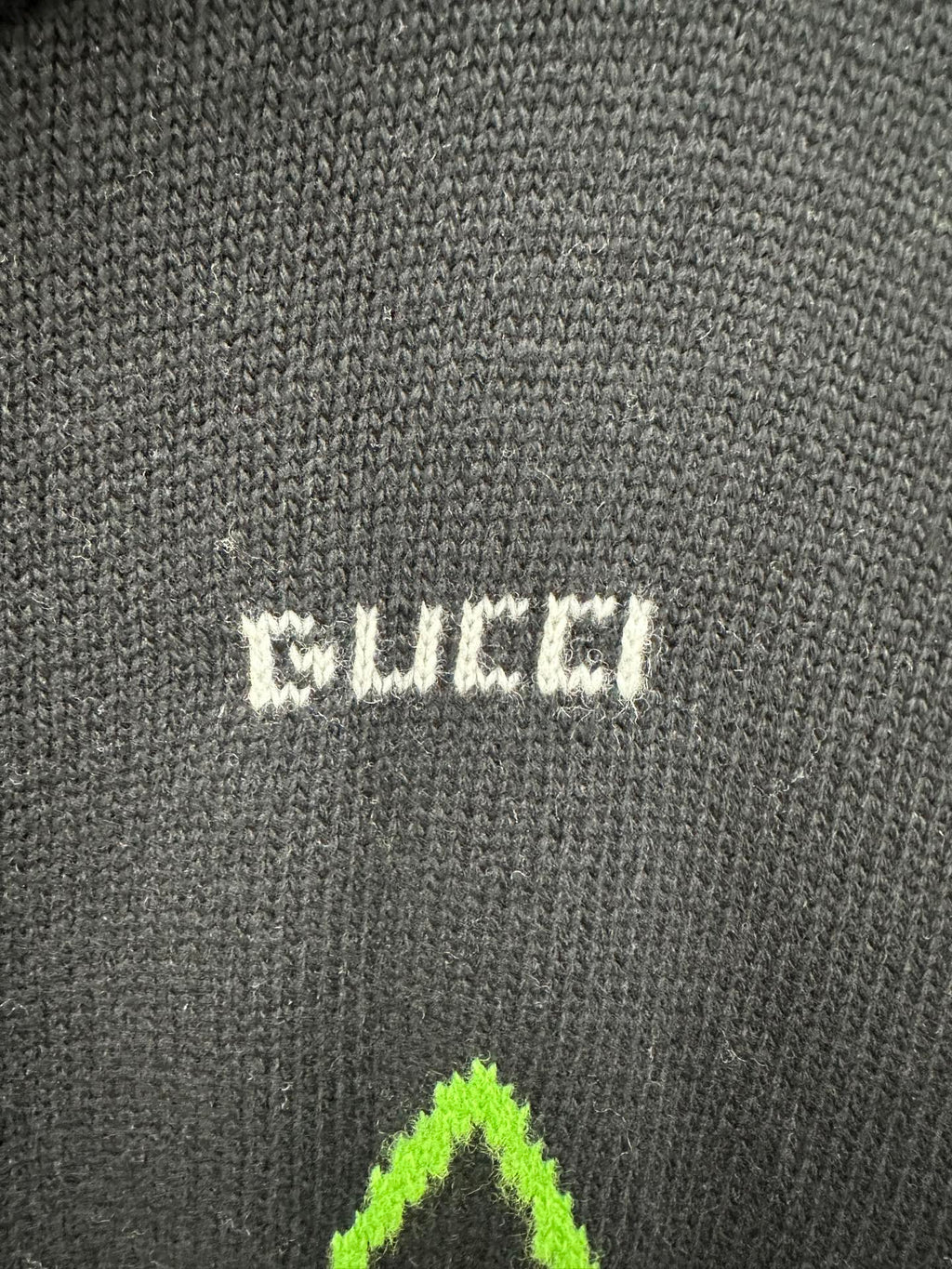 Gucci knit label patch on black fabric with small white and neon green graphic