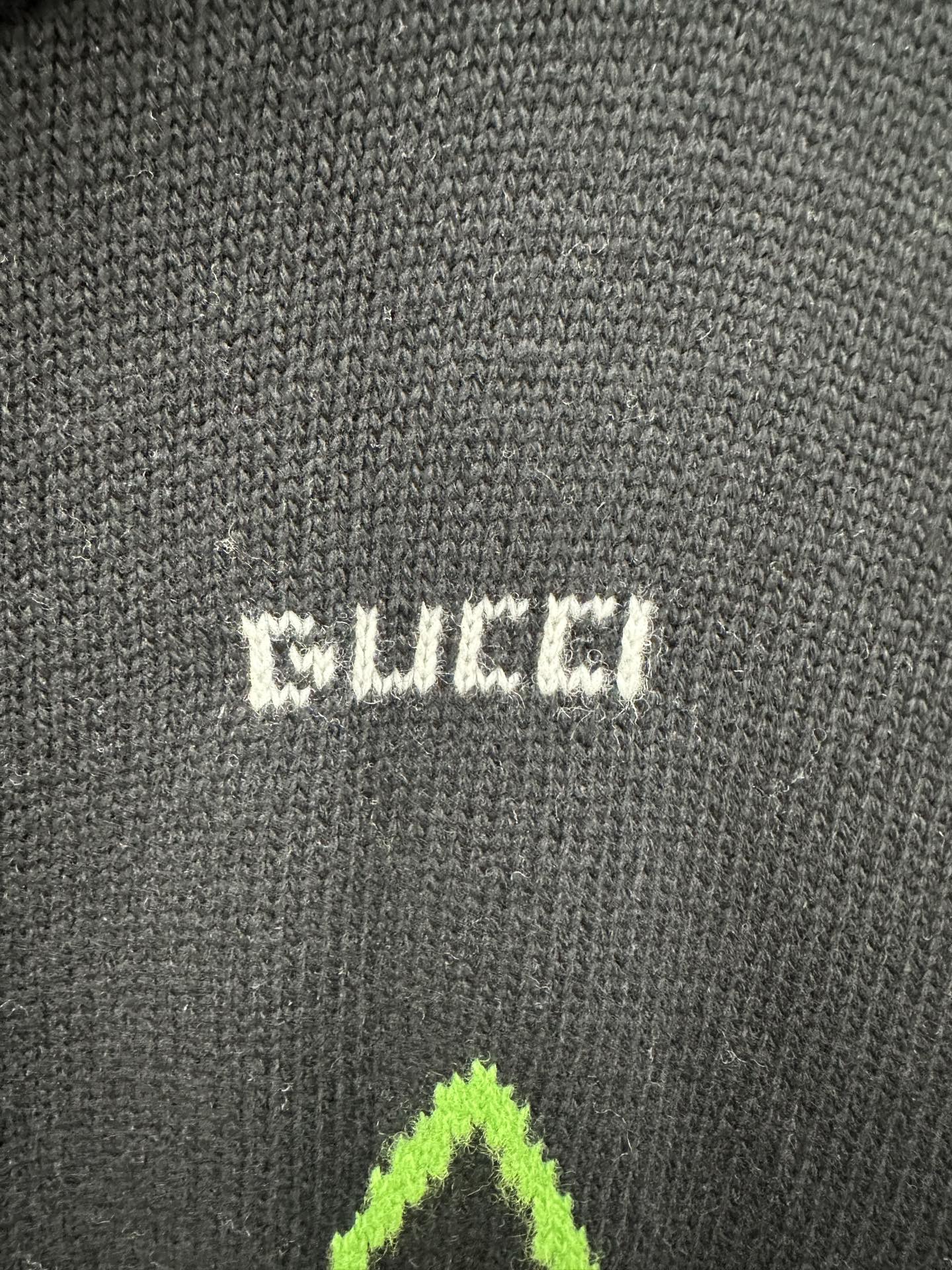 Gucci knit label patch on black fabric with small white and neon green graphic