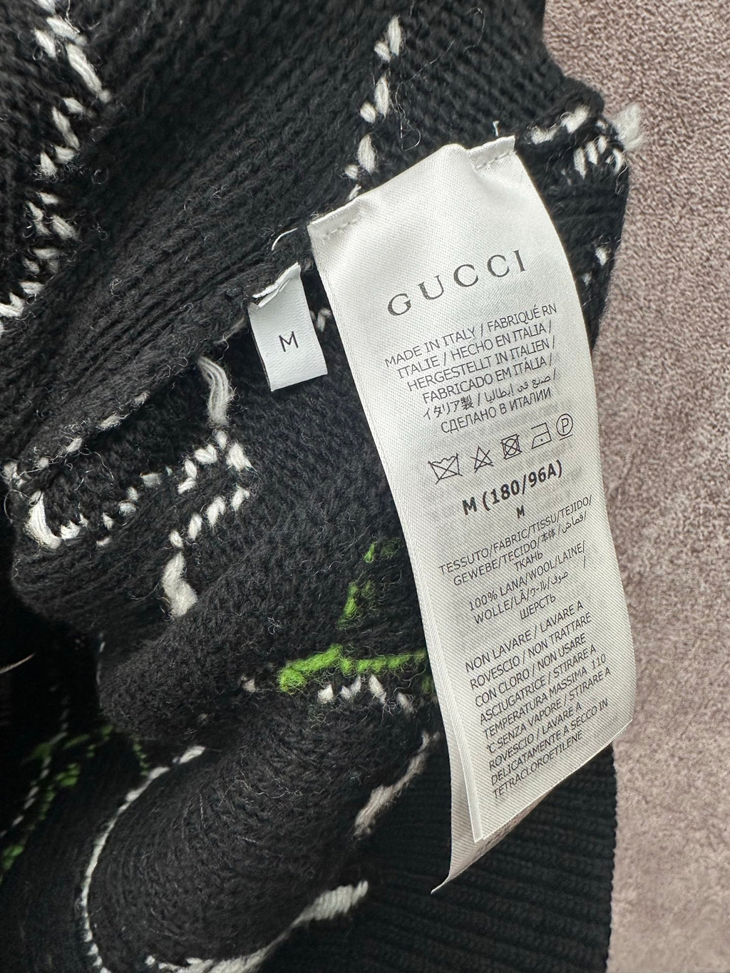 Black knit sweater tag with Gucci label, stitched abstract pattern
