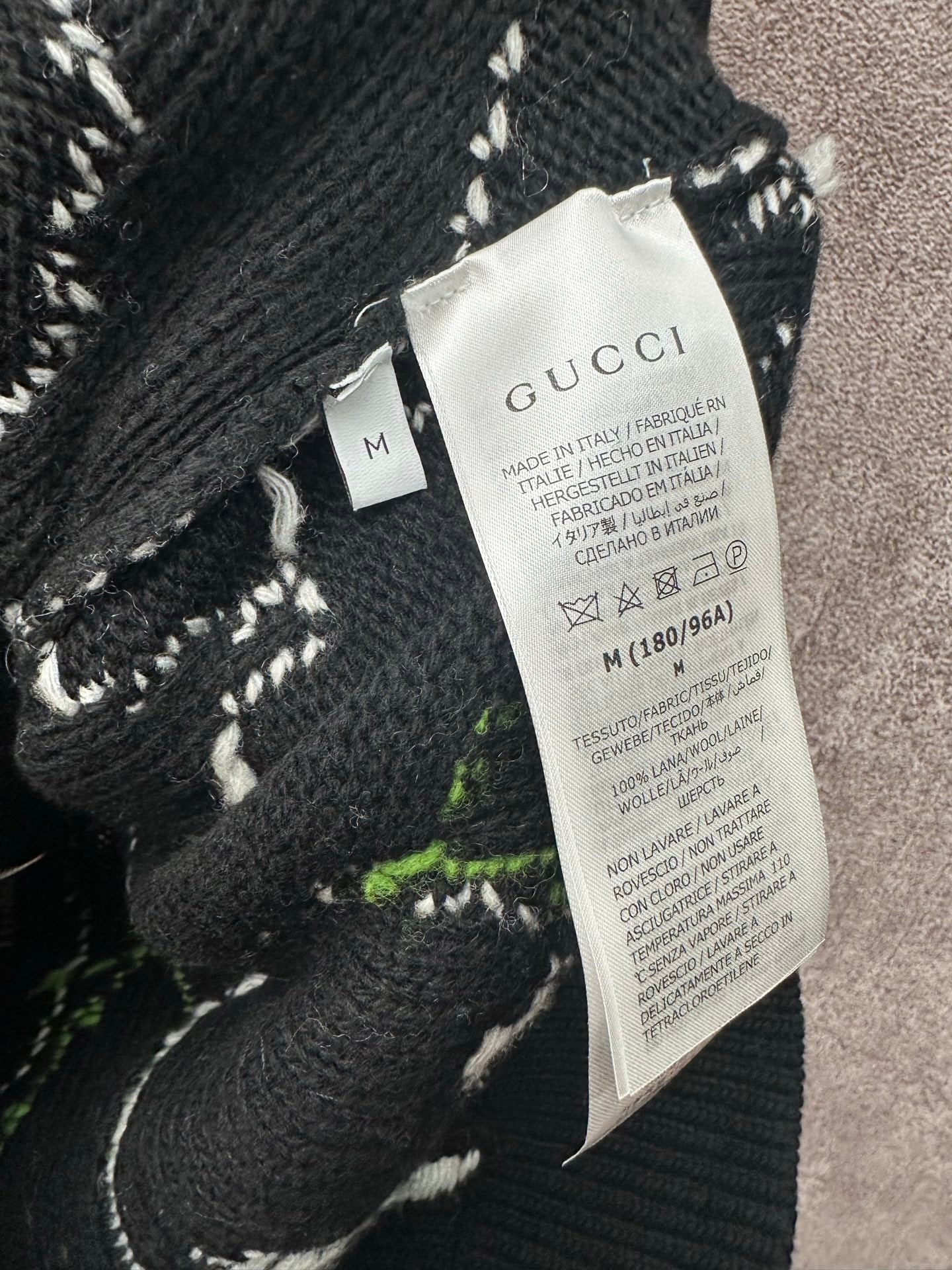 Black knit sweater tag with Gucci label, stitched abstract pattern