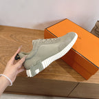 Hermes unisex sneaker held in hand, light gray suede upper with lace-up and white sole