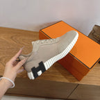 Unisex sneaker in light beige suede with black logo on white sole, held up
