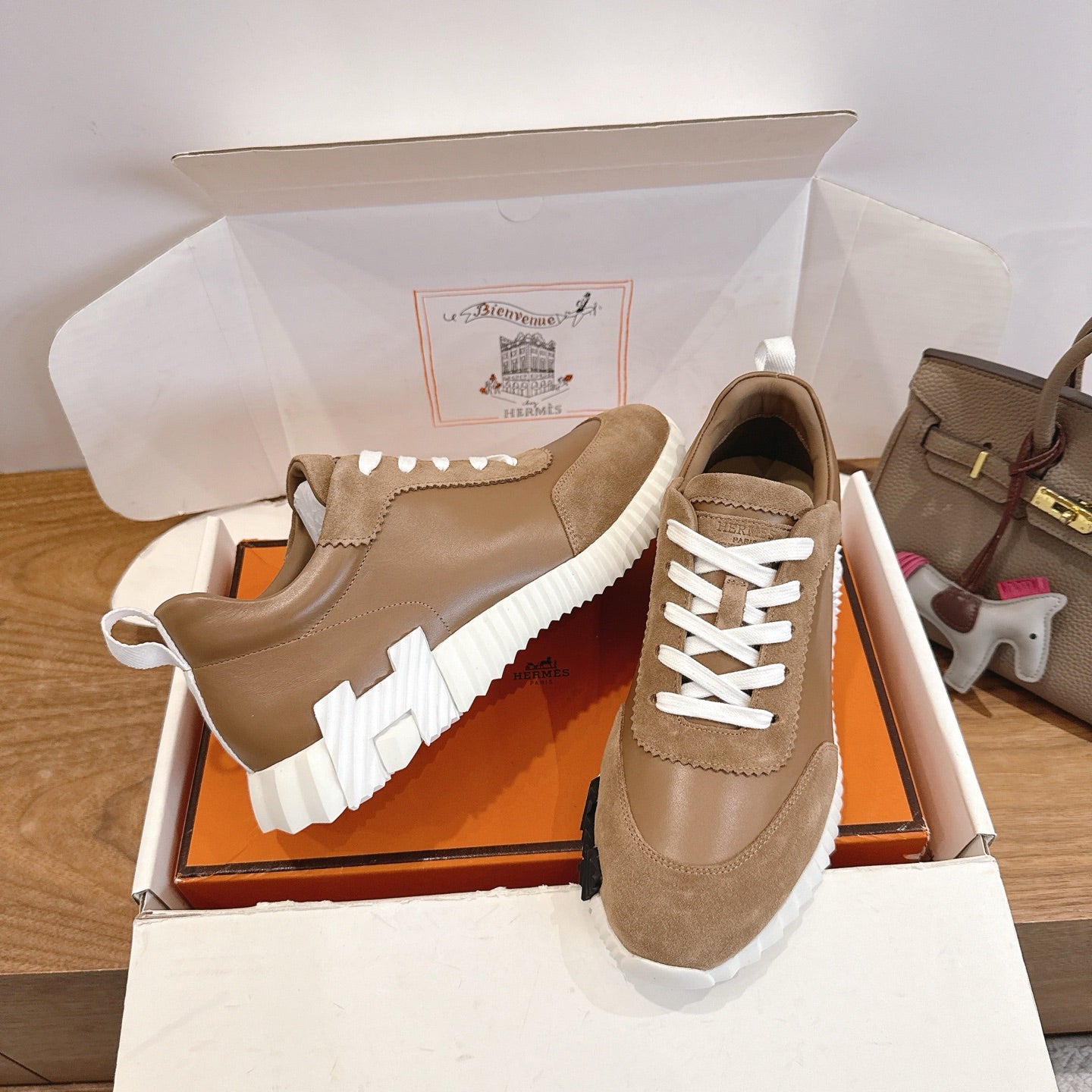 Tan suede sneaker pair in box, featuring white laces and thick white-and-black sole