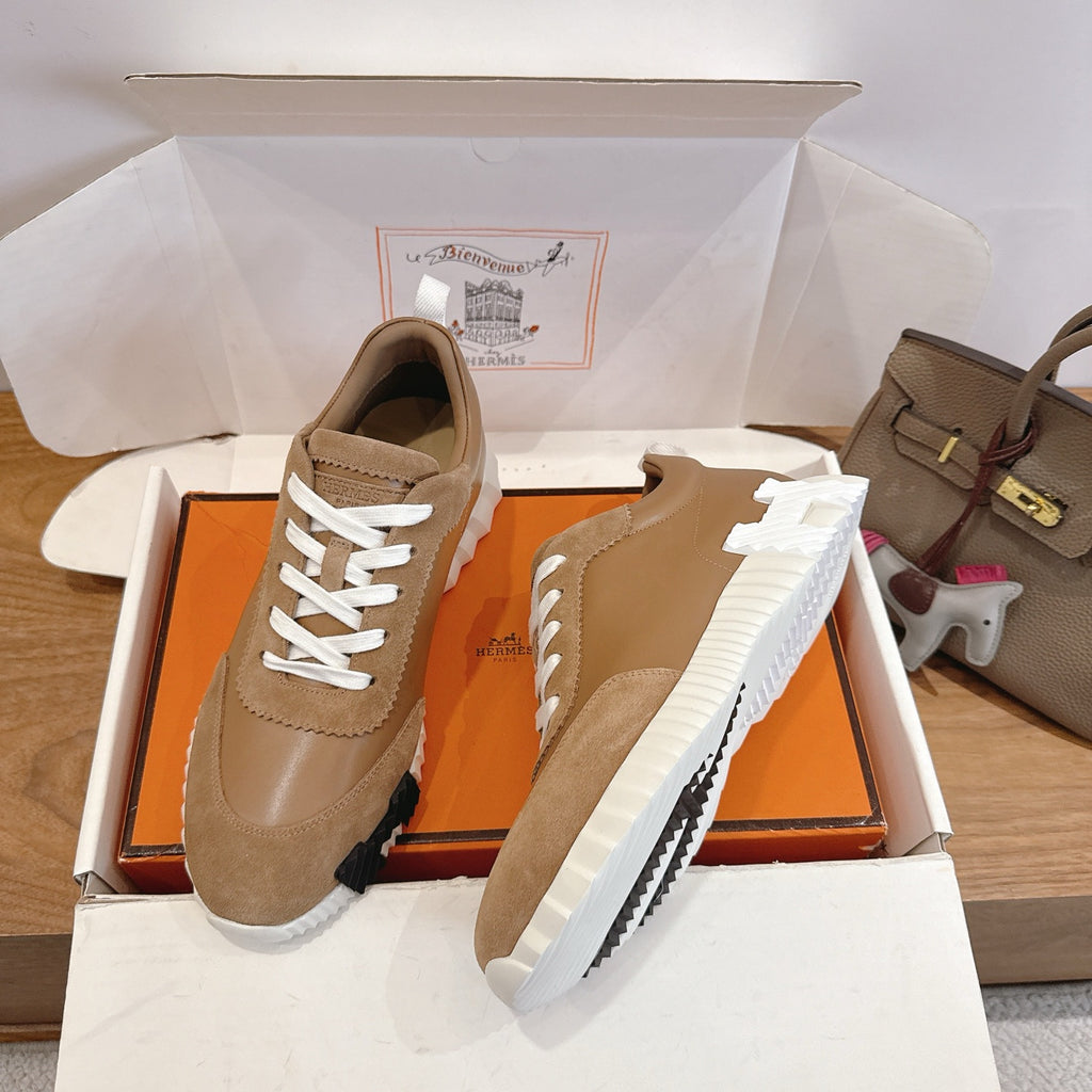 Pair of tan suede sneakers in open box with white laces and chunky ridged sole