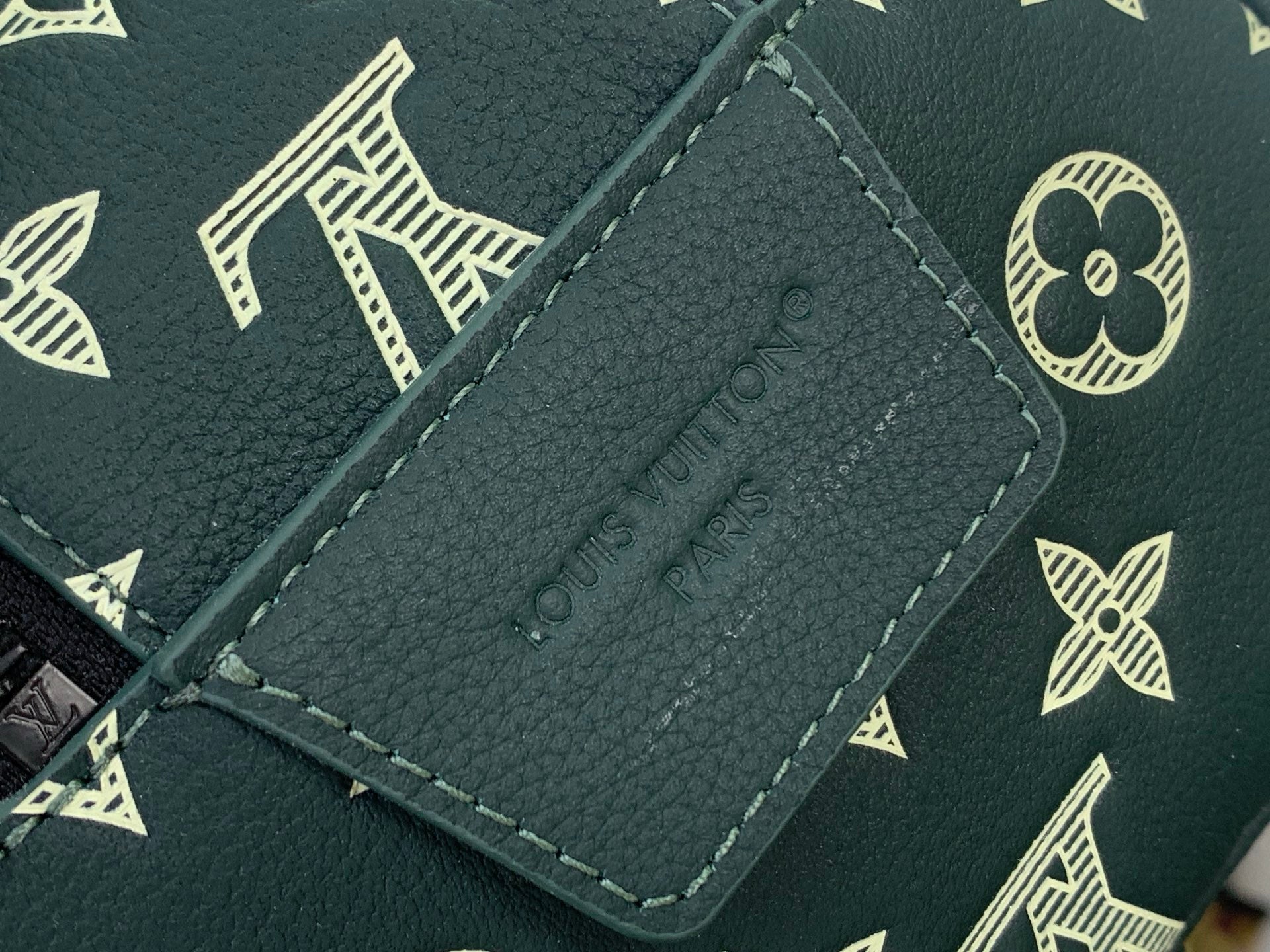 Dark green leather Louis Vuitton tag label with gold stitching detail