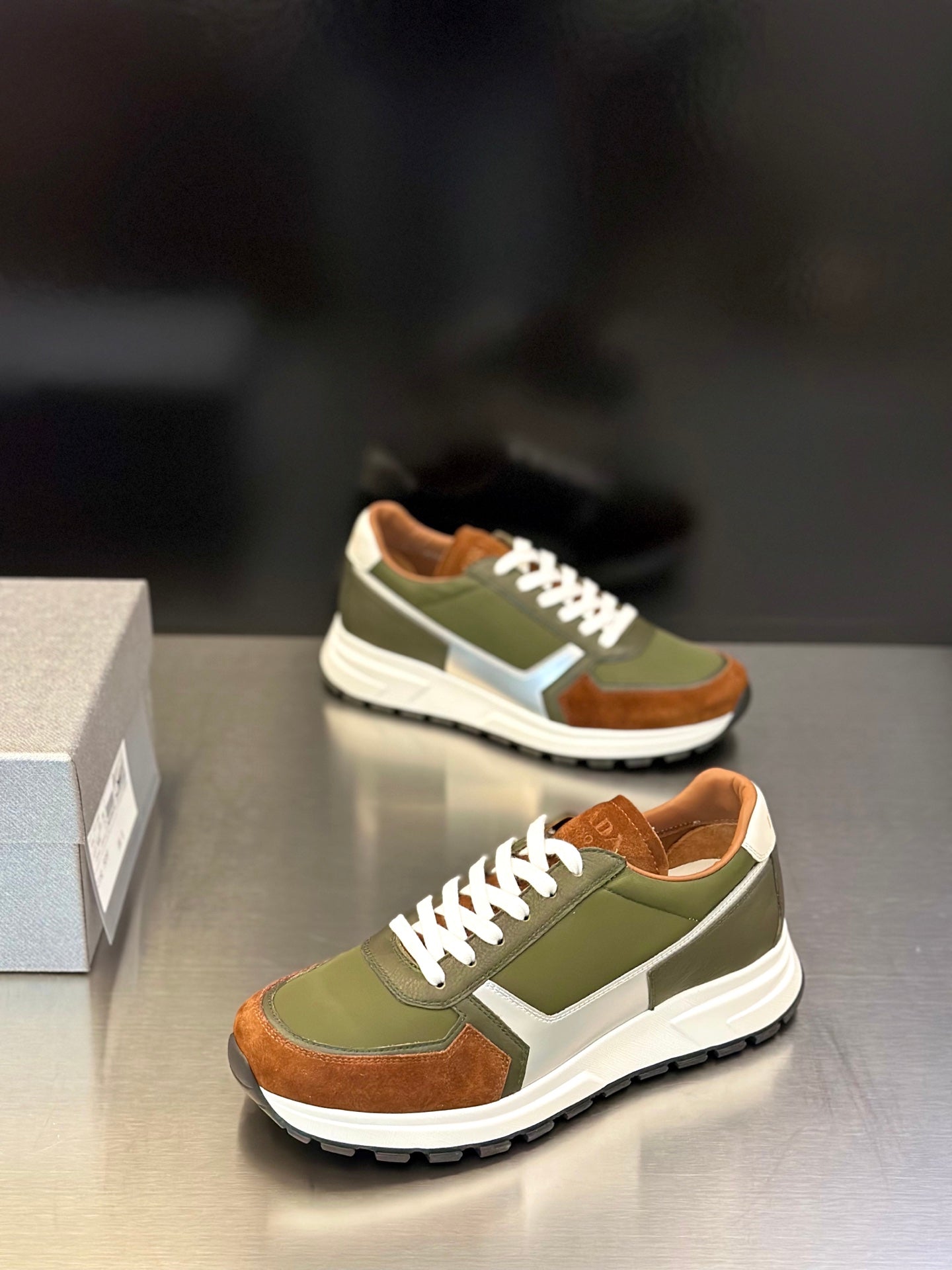 Prada unisex sneakers, angled side view; olive green uppers, brown toe panels, white sole