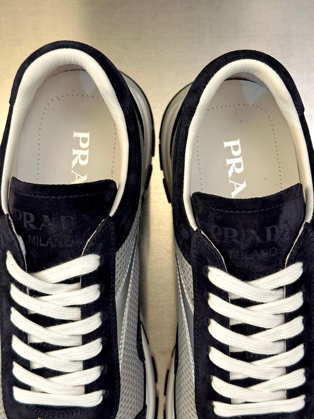 Prada sneakers close-up, dark navy suede, white laces and PRADA lettering on tongue
