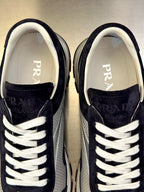 Prada sneakers close-up, dark navy suede, white laces and PRADA lettering on tongue