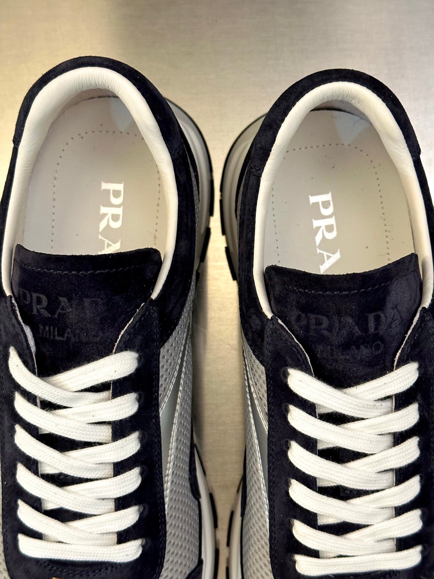 Prada sneakers close-up, dark navy suede, white laces and PRADA lettering on tongue