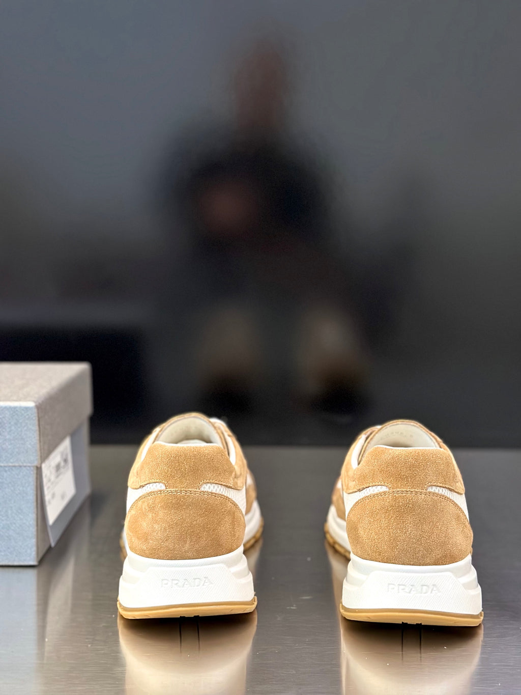 Tan suede sneakers showing back with white heel accents and Prada branding