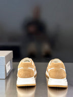Tan suede sneakers showing back with white heel accents and Prada branding