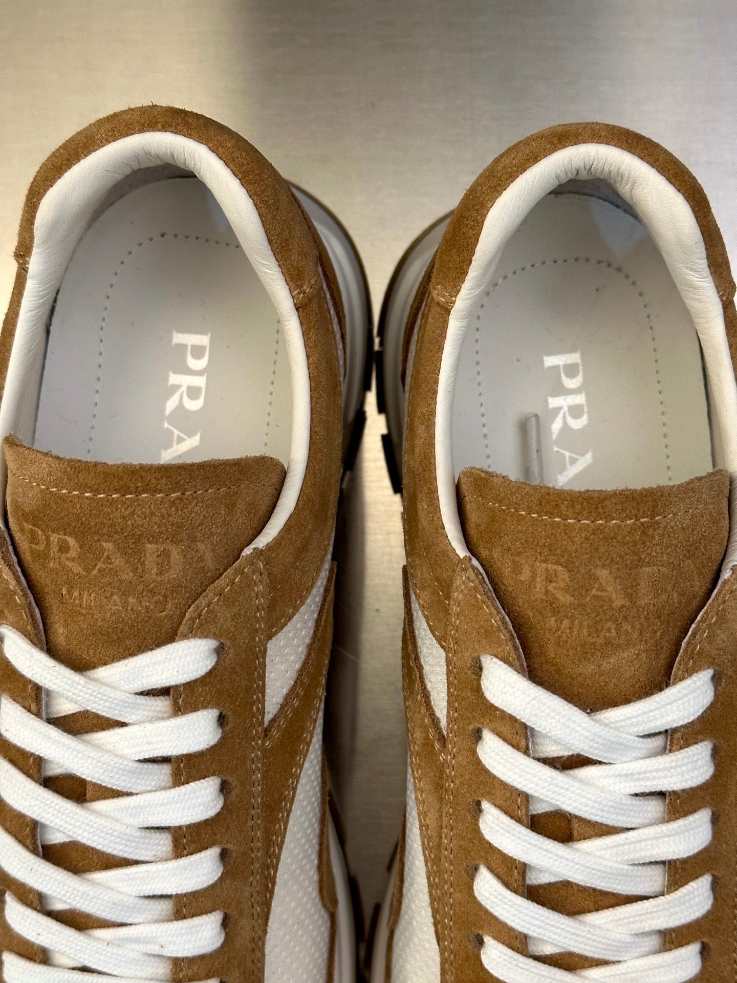 Prada sneakers close-up: tan suede uppers, white laces, logo on inner lining