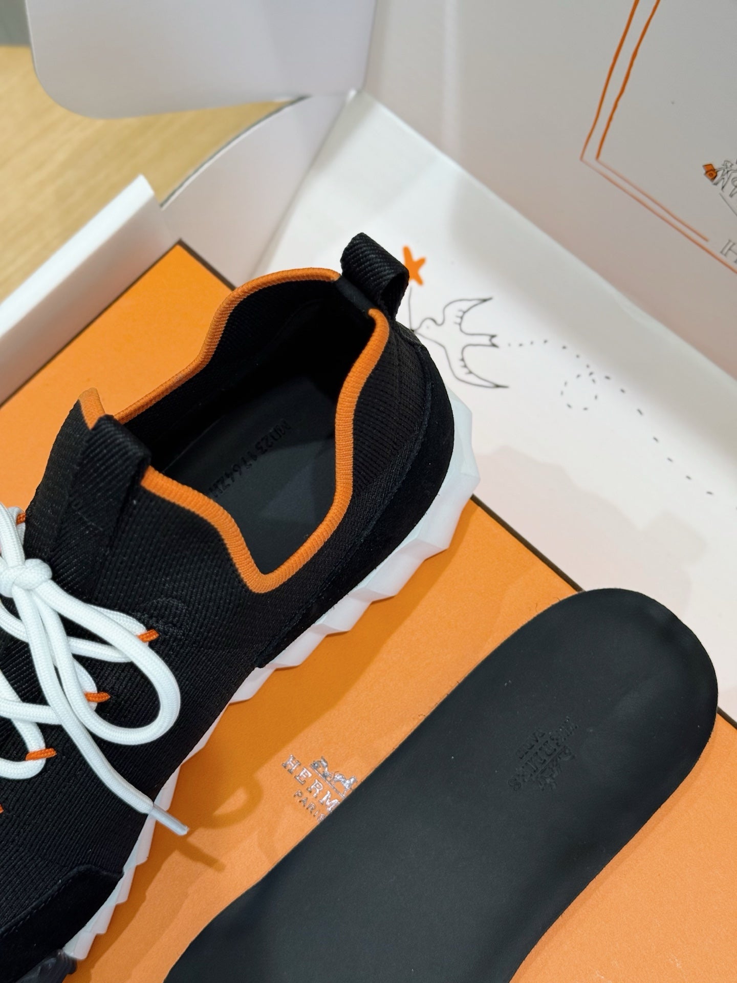 Hermes unisex sneakers side view, black upper with orange trim, white laces, chunky sole