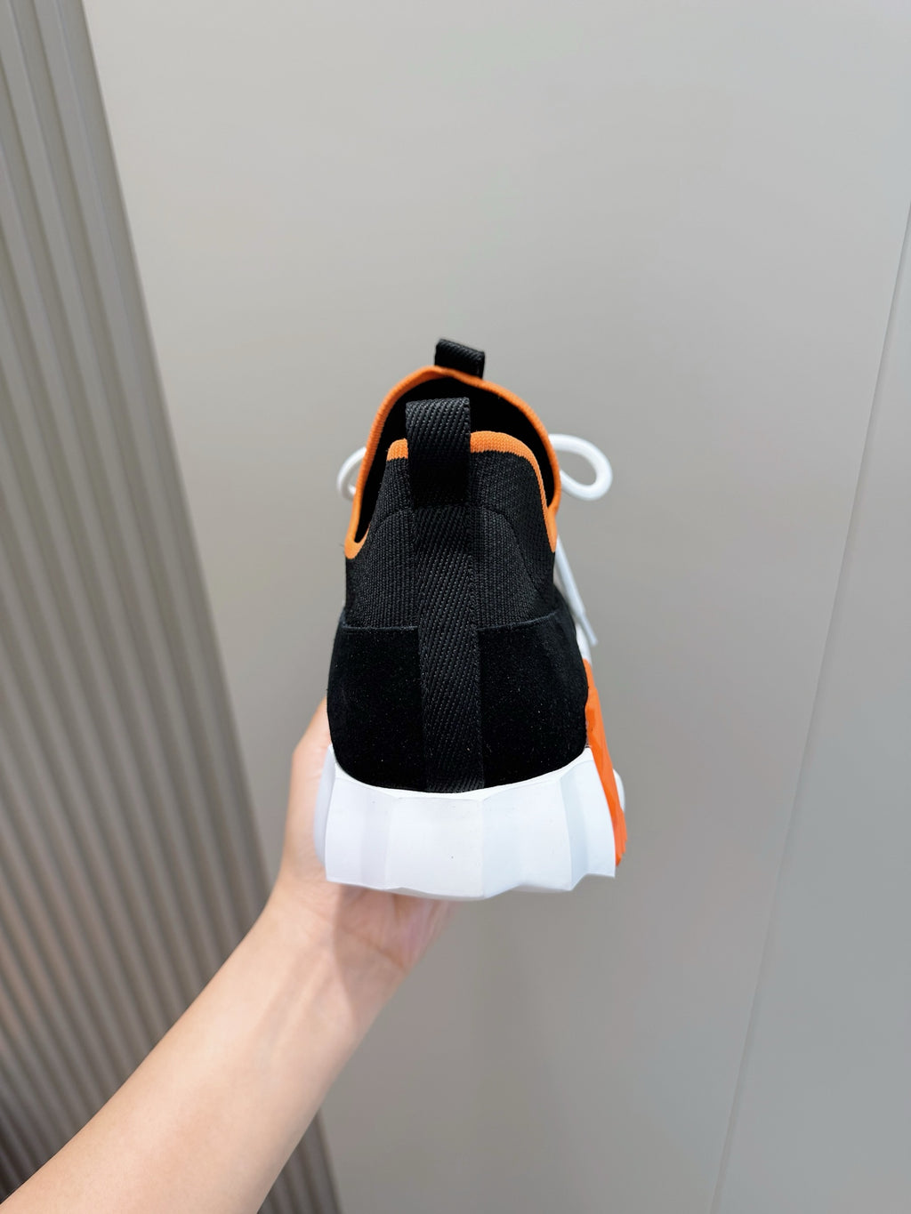 Hermes unisex sneakers heel view, black knit with orange collar, white outsole