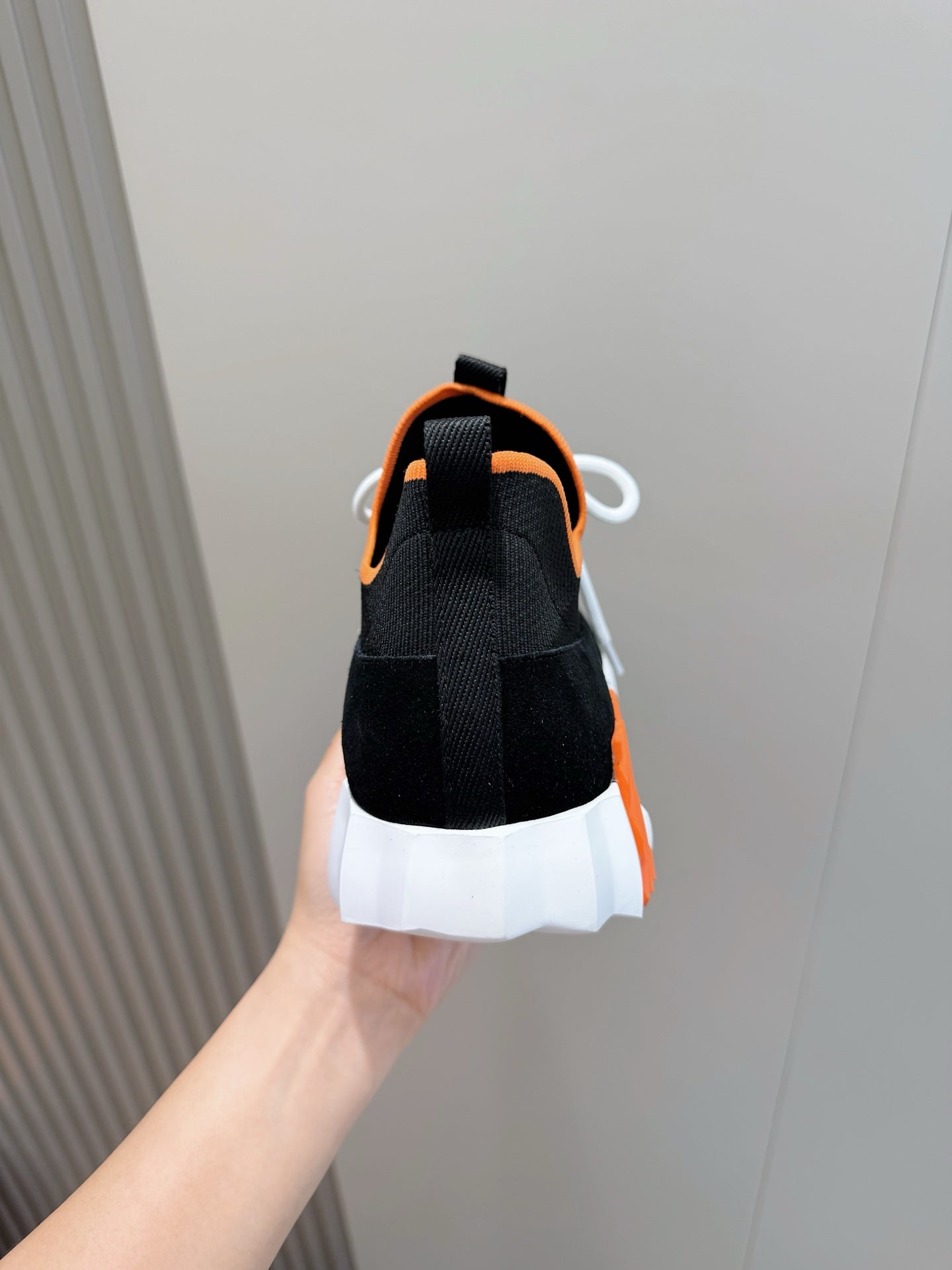 Hermes unisex sneakers heel view, black knit with orange collar, white outsole