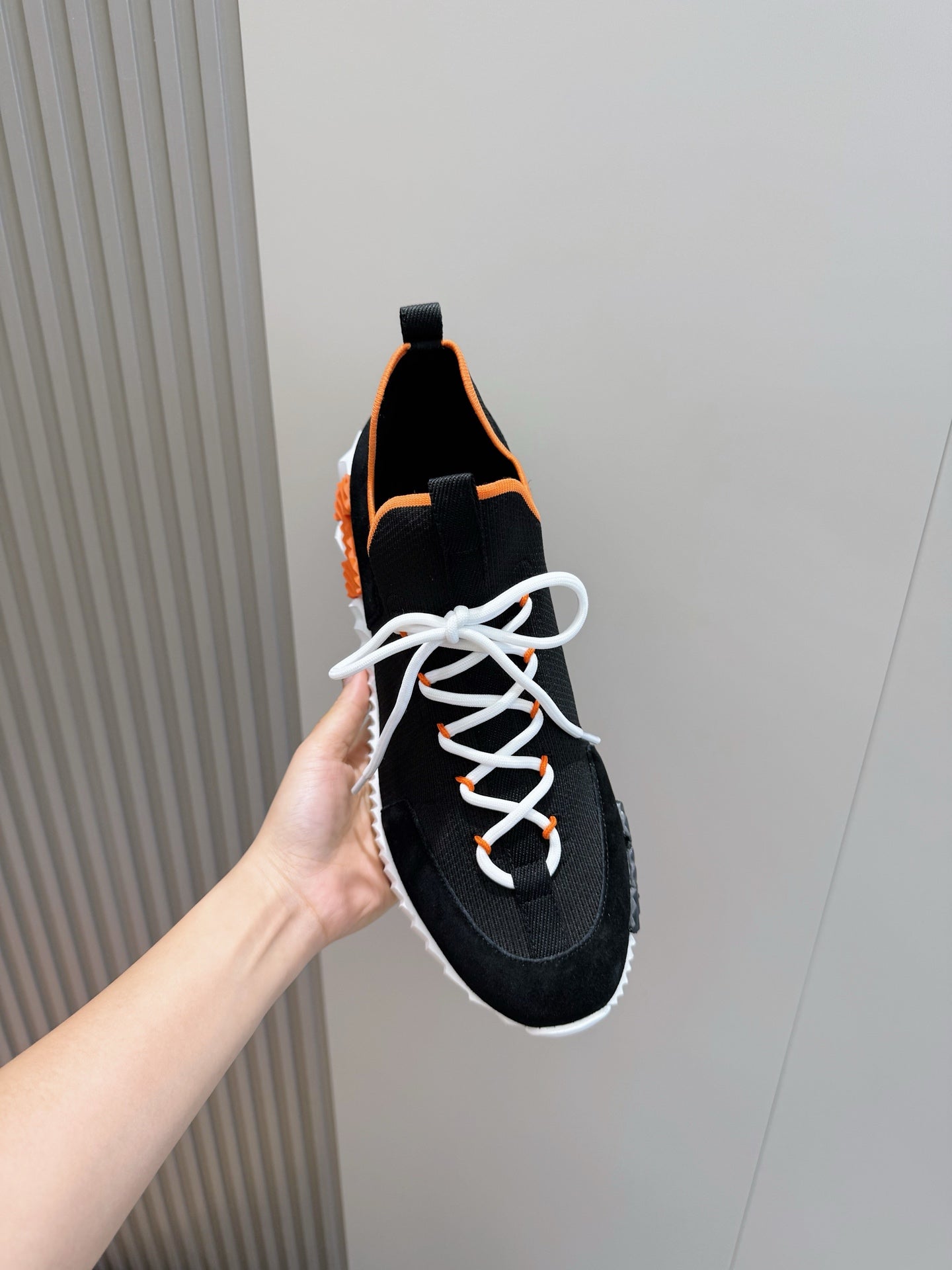 Hermes unisex sneakers close-up, black fabric with orange lining, white laces and midsole