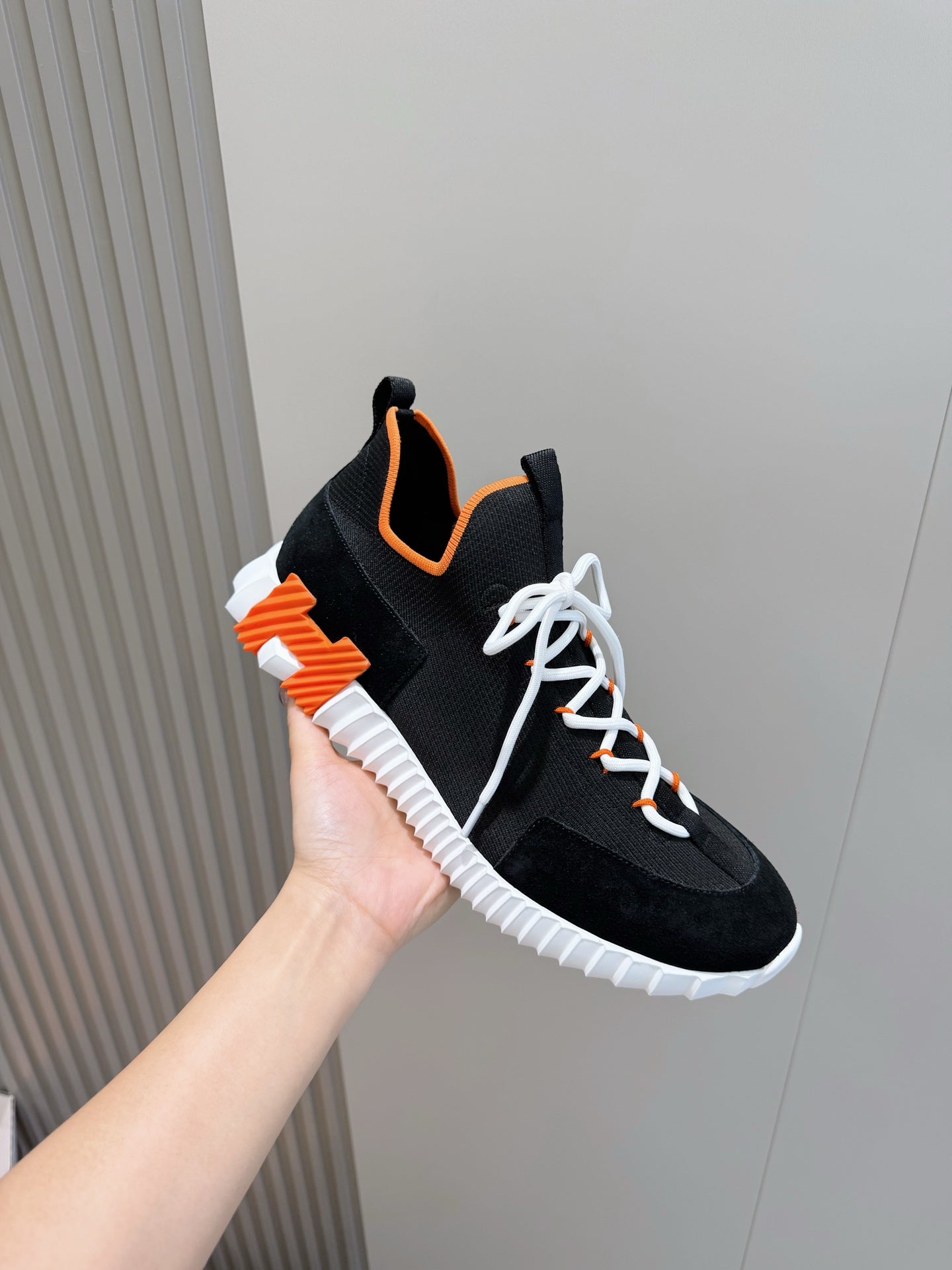 Hermes unisex sneakers held up, black with orange accents, white laces, textured white sole