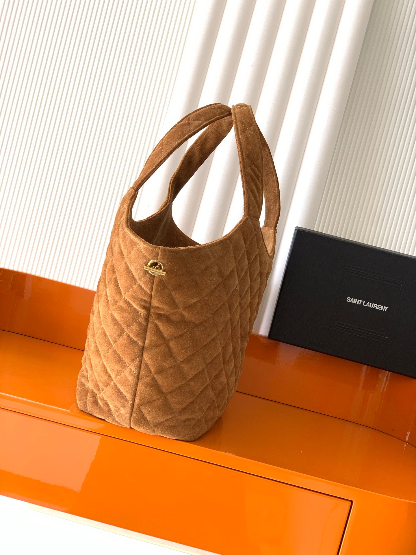 Quilted tan handbag with short handle and gold logo plate on front