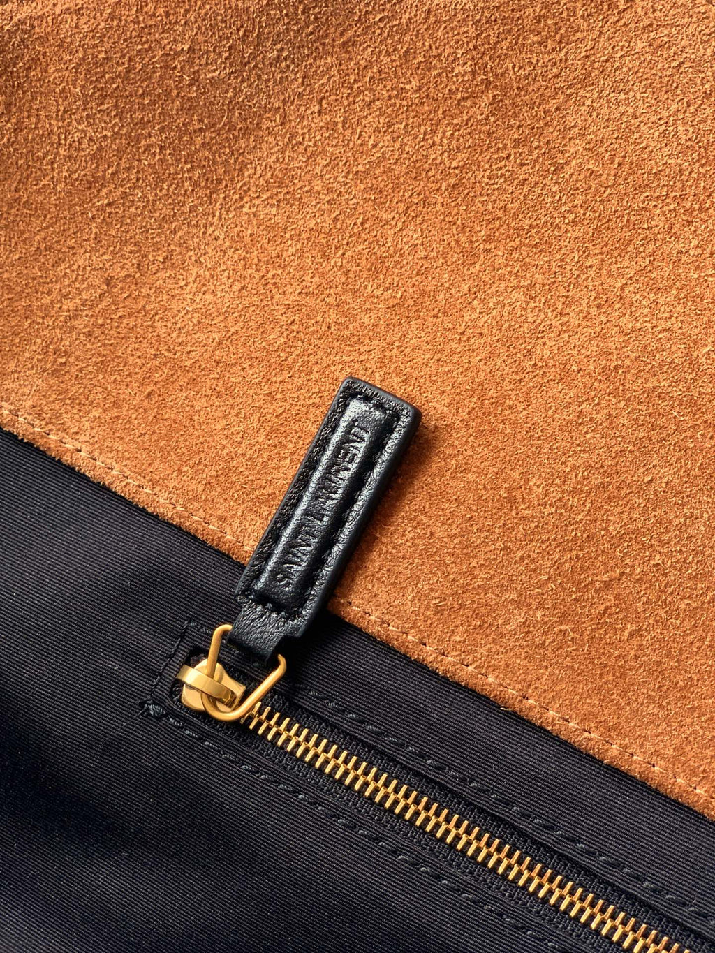 Tan suede and black zipper area with gold zipper pull on handbag