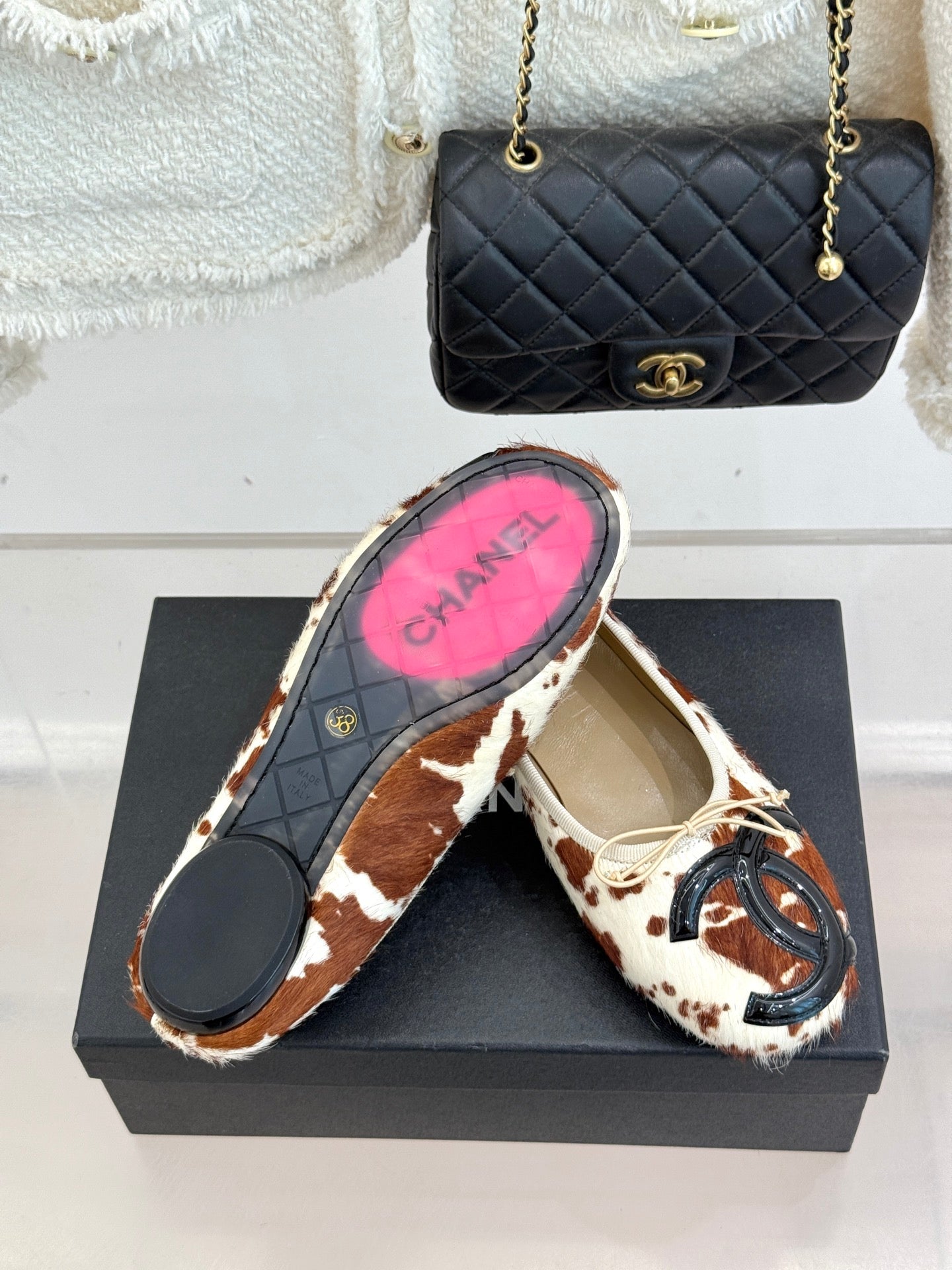 Cow-print ballet flats with cream laces on black shoebox, sole view included
