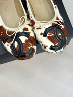 Close-up of cow-print ballet flats with cream laces and metal hardware