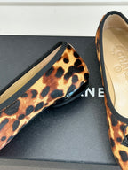 Close-up of leopard-print flats with black logo buckle detail and textured trim.