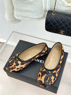 Leopard-print flats with black oval logo embellishment and beige insole lining.