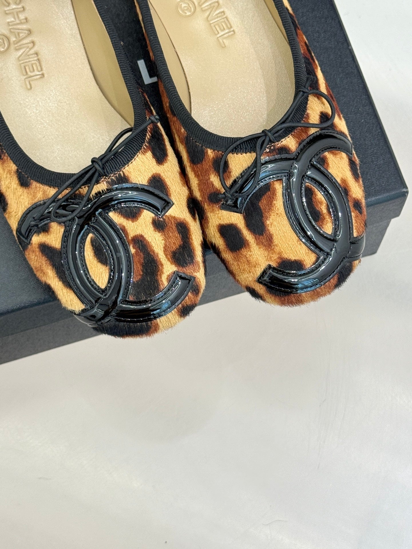 Close-up of leopard-print flats with black oval logo embellishment and lace-up ties.