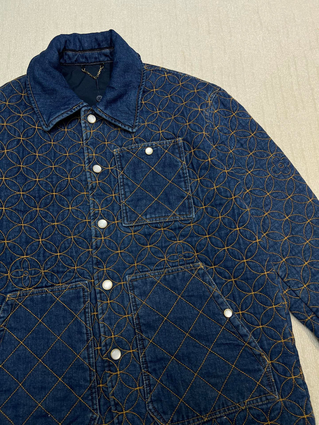 Denim jacket with blue-and-gold lattice embroidery, chest patch, buttoned pockets