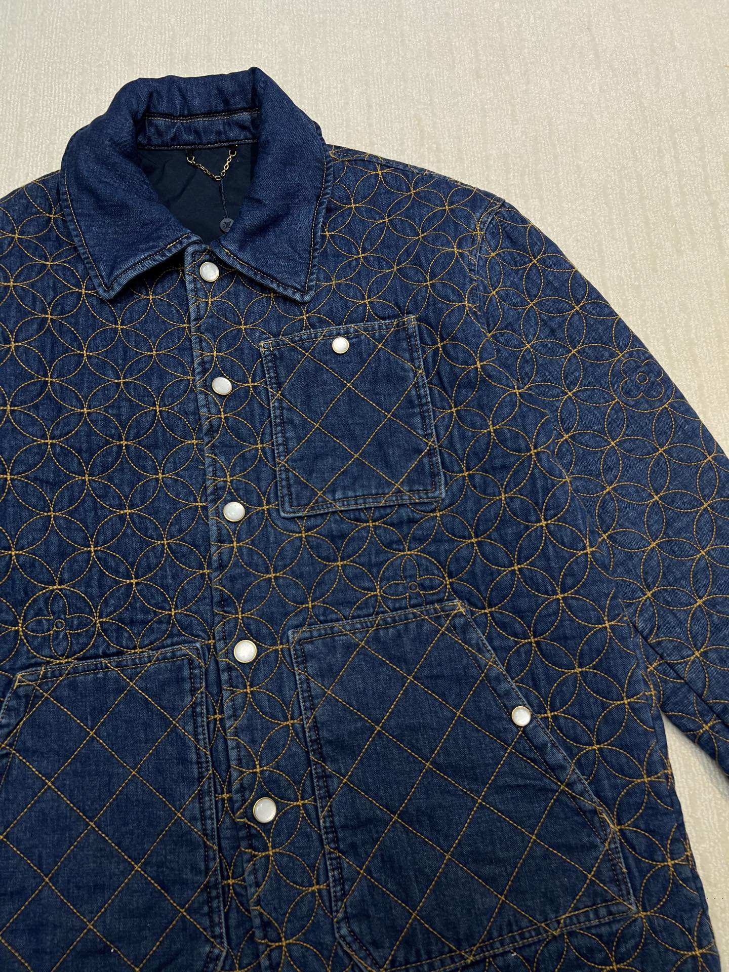 Denim jacket with blue-and-gold lattice embroidery, chest patch, buttoned pockets