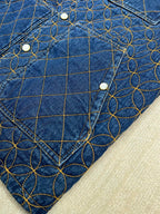 Denim jacket sleeve with blue-and-gold lattice embroidery and metal button