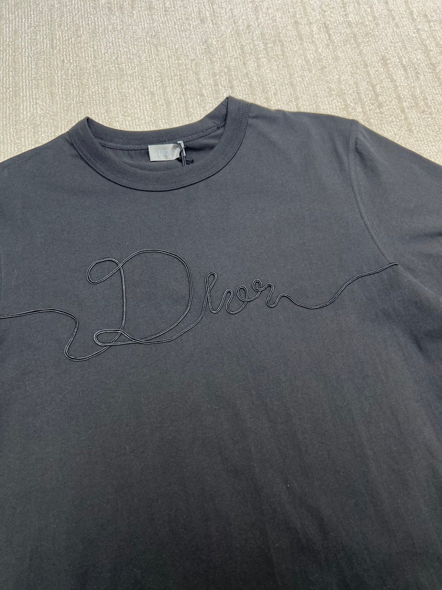 Dior T-shirt front close-up, dark; embroidered Dior script across chest