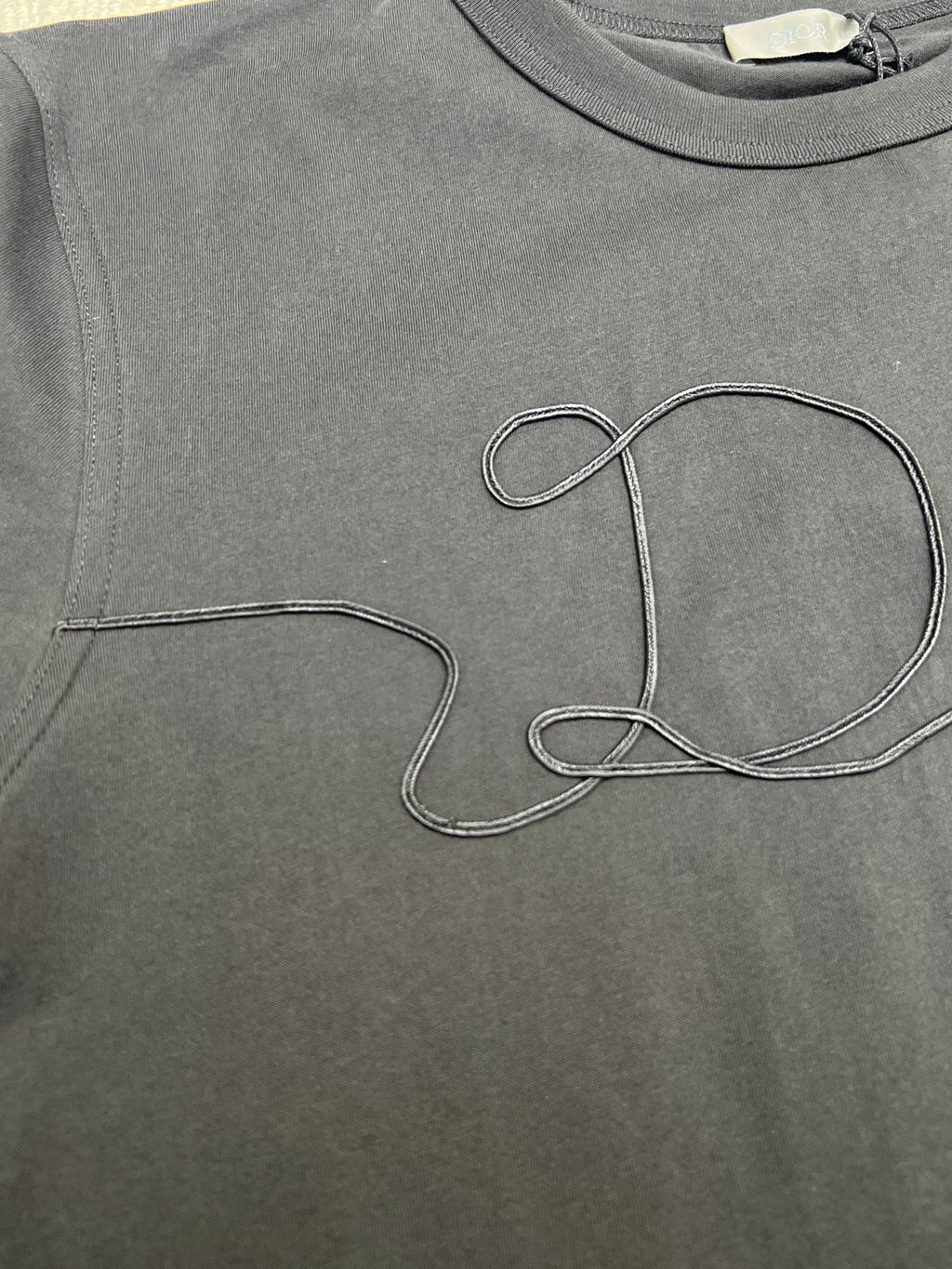 Dior T-shirt chest close-up, dark; large outlined Dior script embroidery