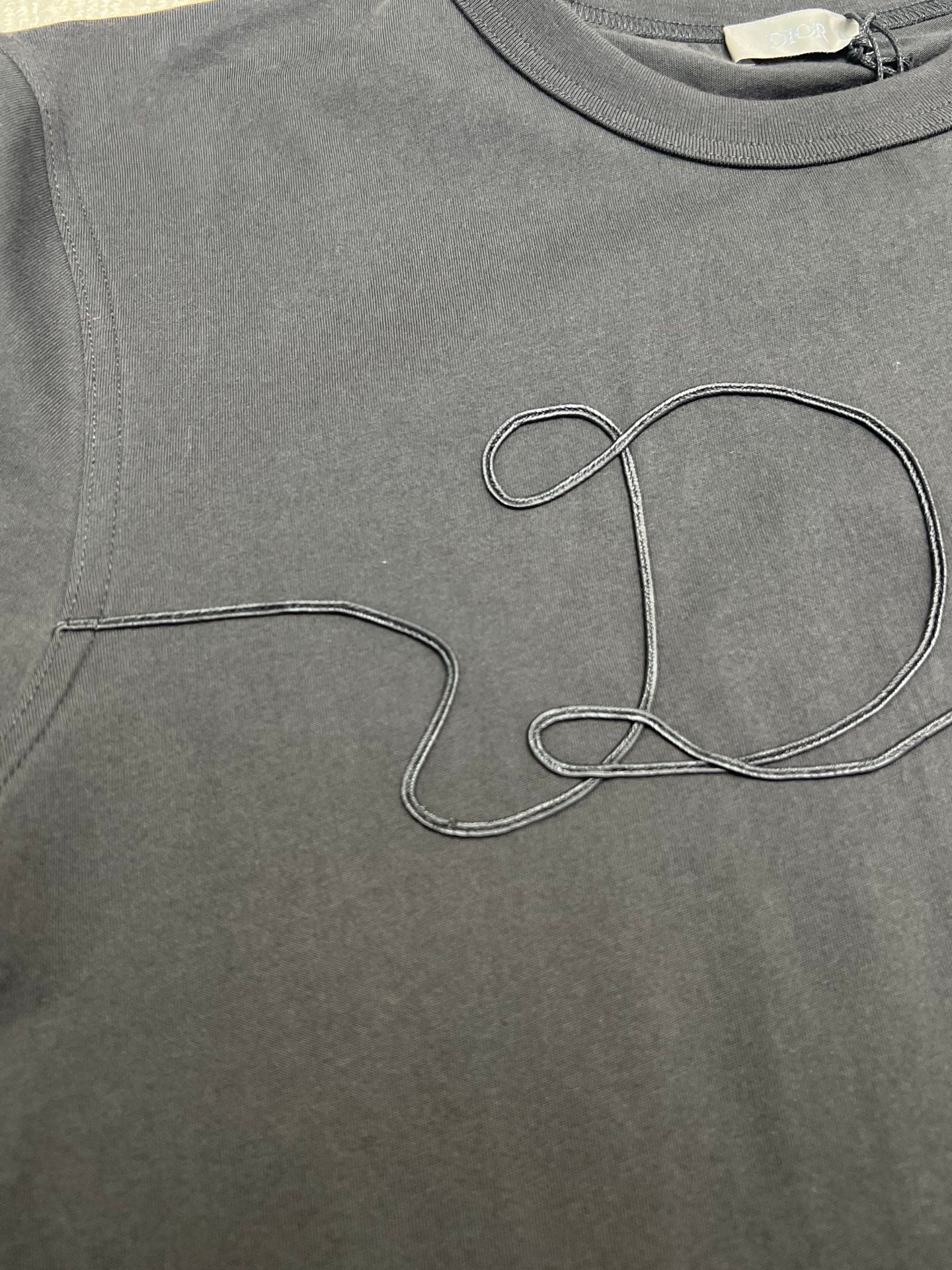 Dior T-shirt chest close-up, dark; large outlined Dior script embroidery