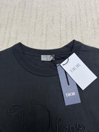 Dior T-shirt front close-up, dark crew neck; embroidered Dior script outline