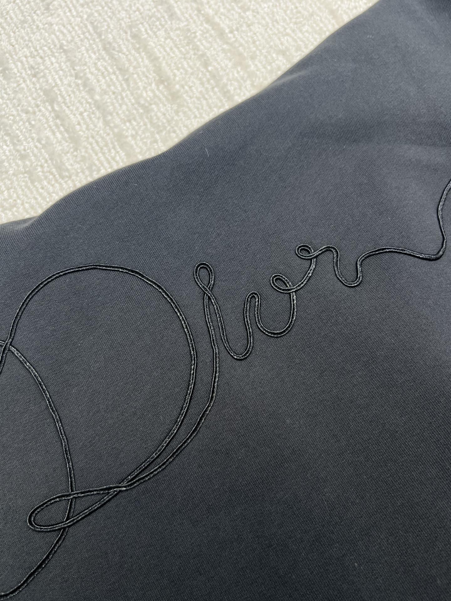 Dior hoodie logo embroidery on dark navy fabric close-up, partial lettering visible
