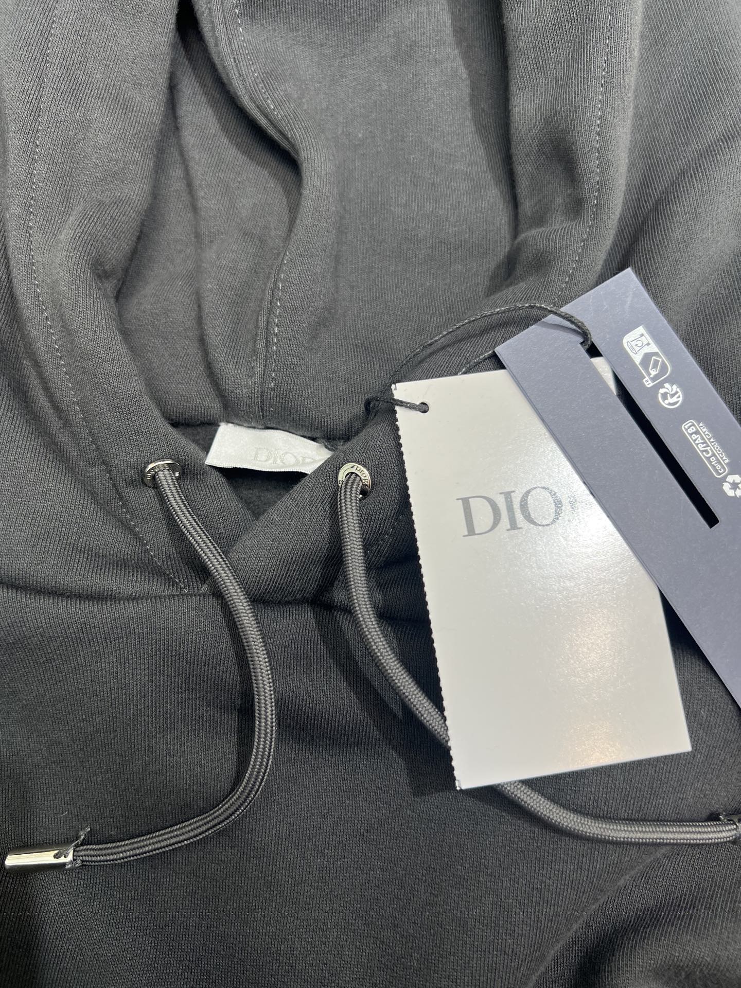 Dior hoodie detail with gray drawstring cord and interior pocket seam; attached tags